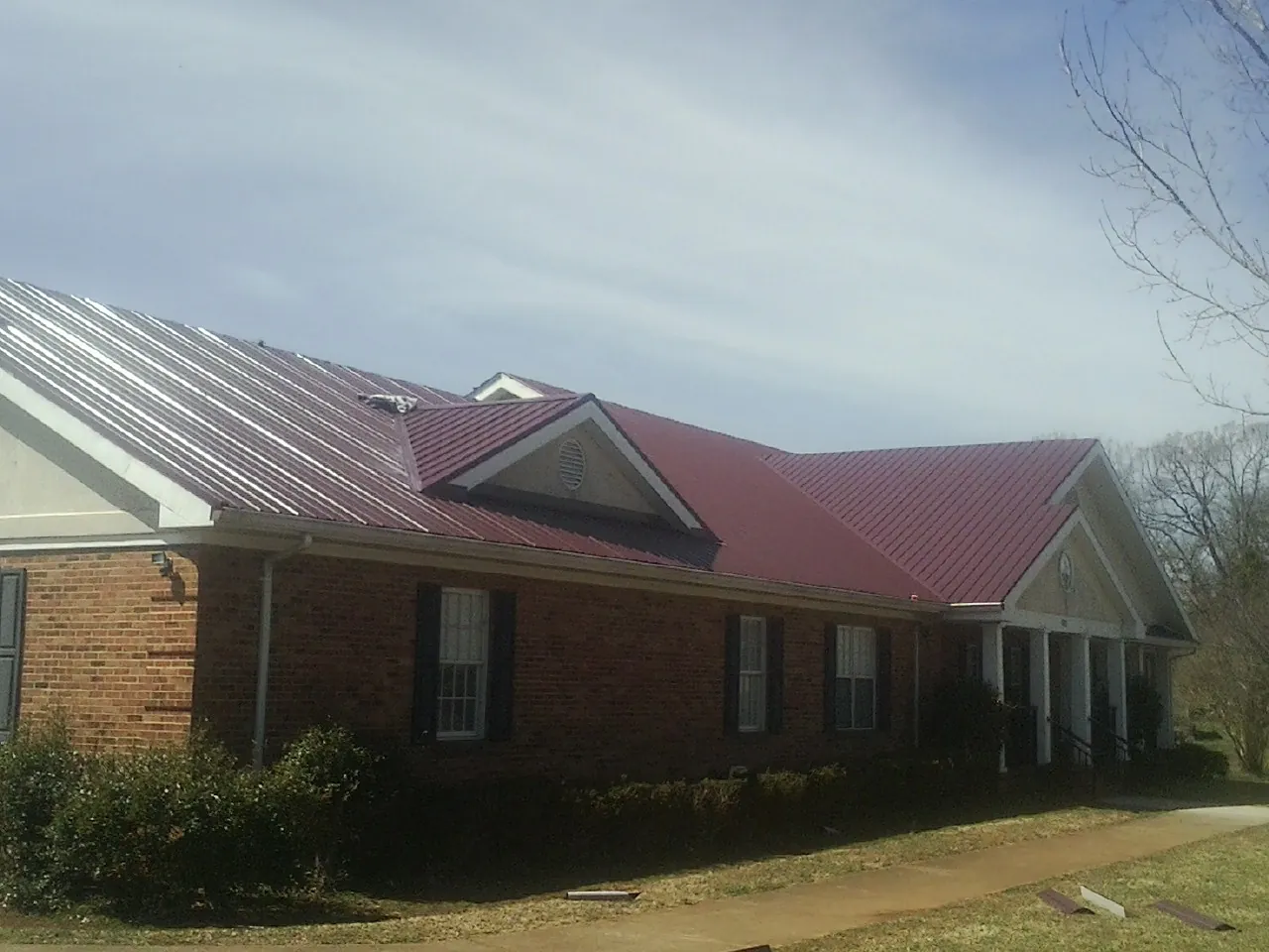 Red metal roof with gabled entries on a long brick building, from a Hail Damage Roof Repair job in Dracut