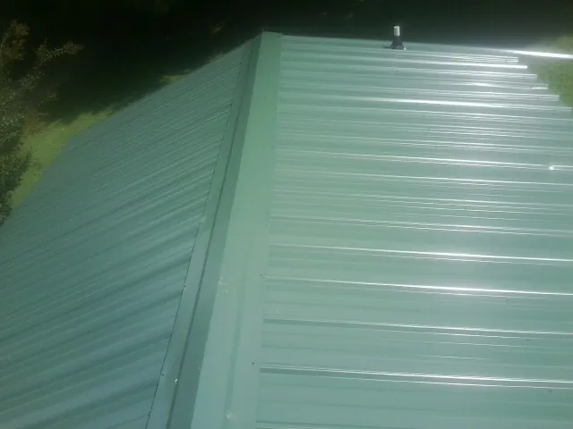 New green metal panels meeting at the ridge of a roof — Flat Roof Repair work by our crew in Dracut