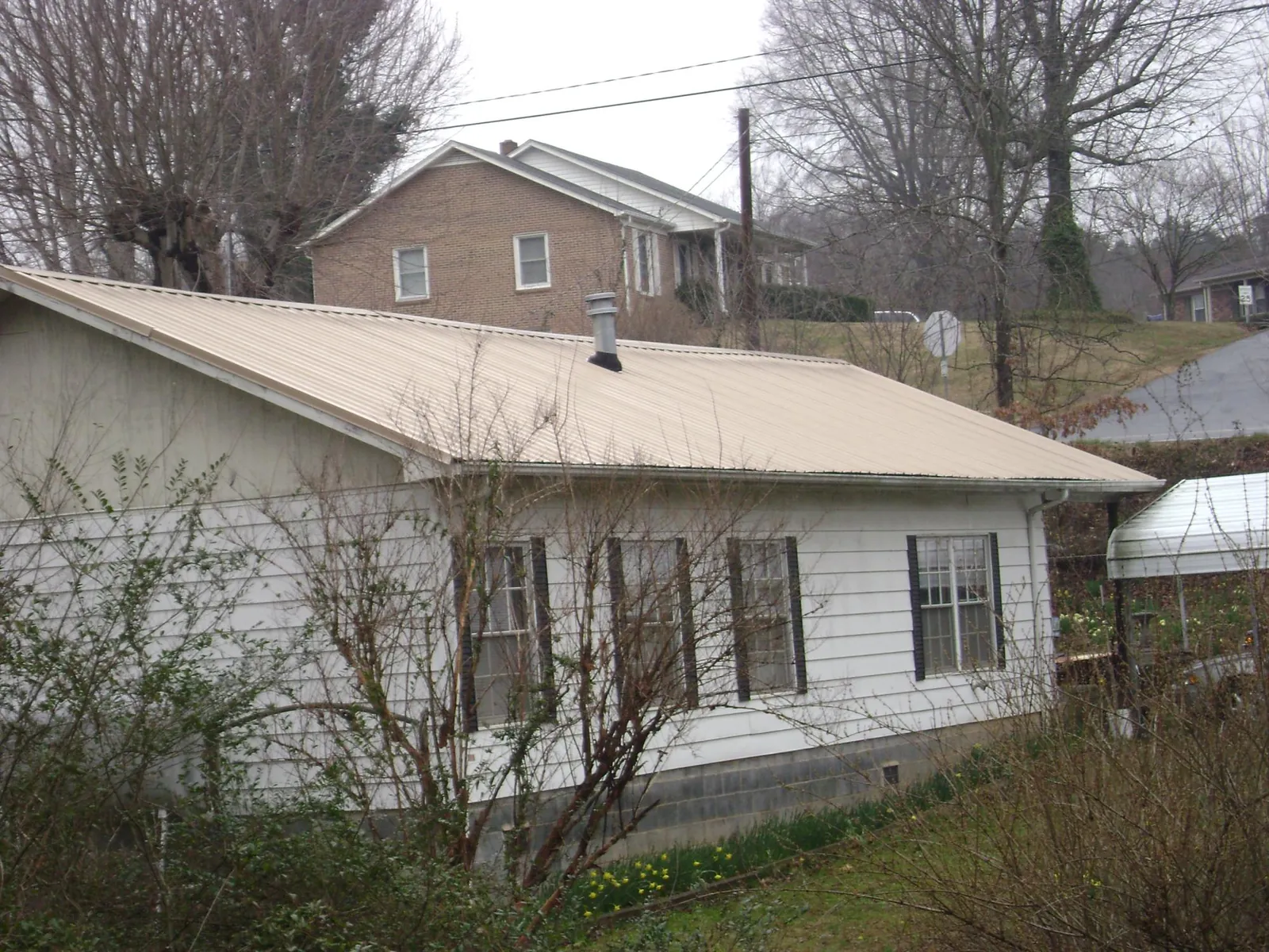 Tan metal roof on a white sided house set into a hillside — Commercial Roofing by Roofing Brothers in Dracut