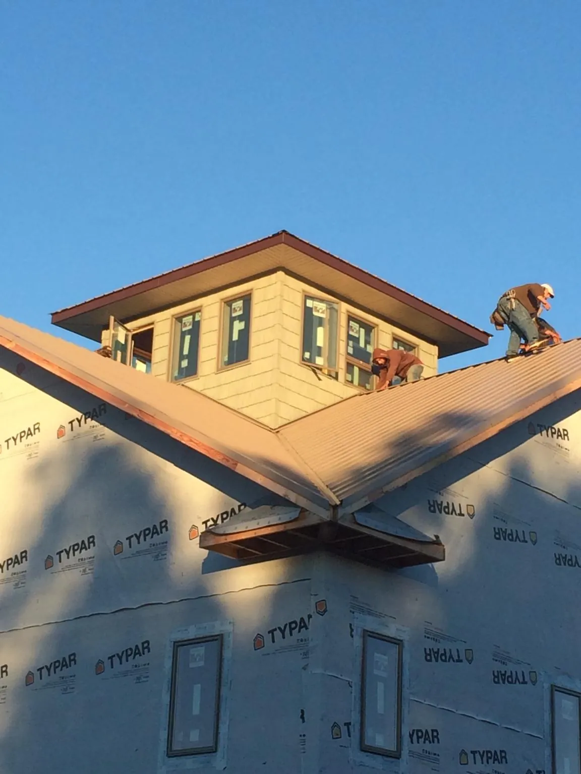 Roofers working around a rooftop cupola on a new metal roof at sunset — Roof Waterproofing in Dracut by Roofing Brothers